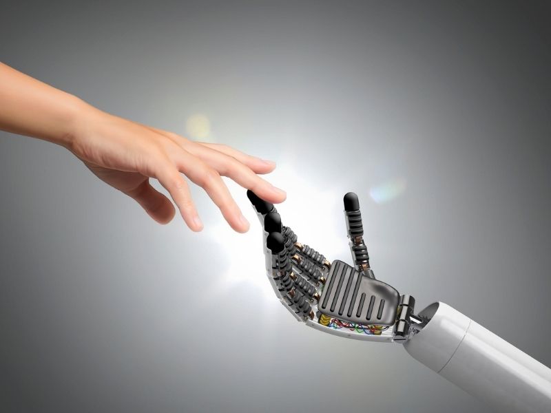 Mano humana se acerca a una mano robótica como representación de la colaboración entre personas e inteligencia artificial.