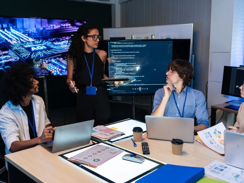 Equipo de profesionales analiza herramientas de inteligencia artificial y datos en computadoras dentro de una oficina.